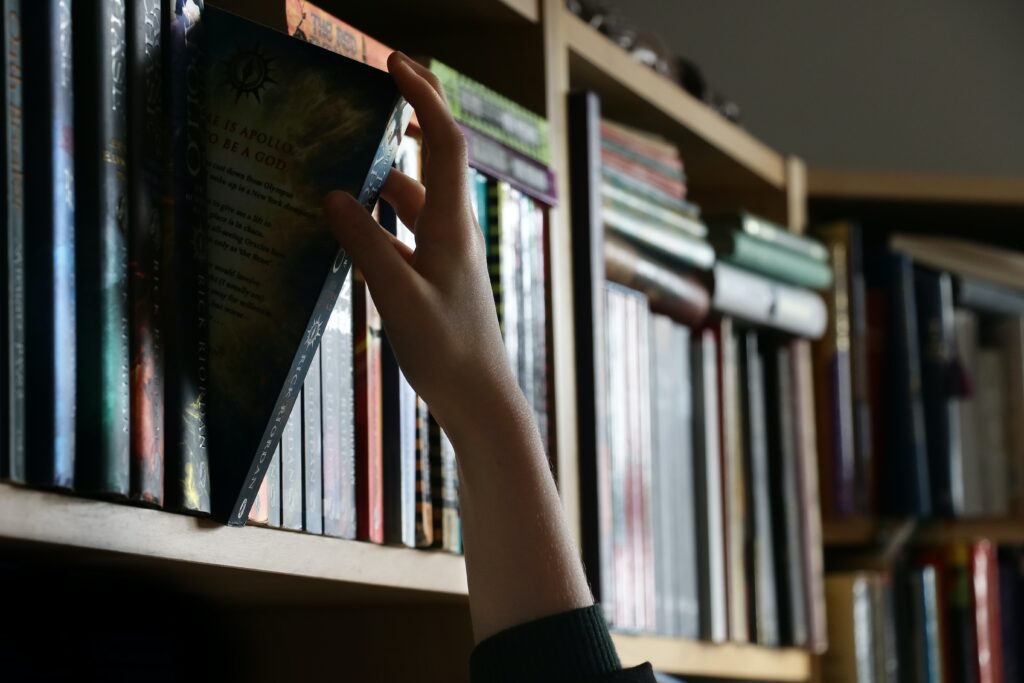 photo of a hand reaching for a book on a bookshelf